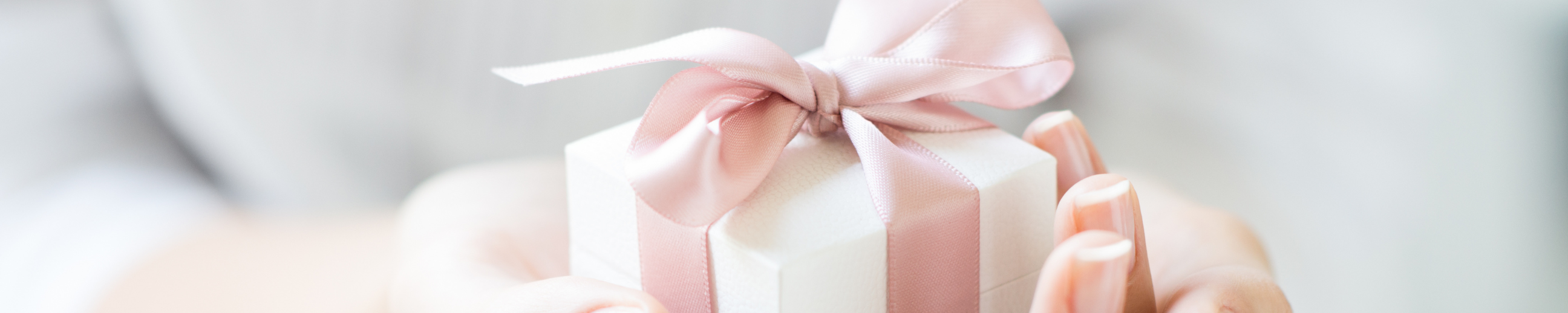 Zwei Hände halten ein weißes Geschenk mit rosa Schleife