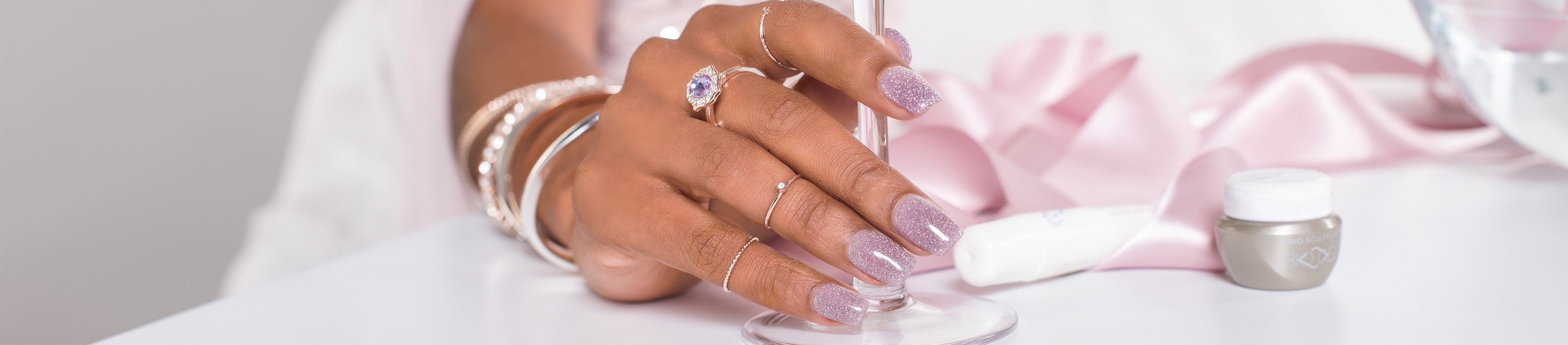 Eine Frau mit Glitzernägeln hält den Stiel eines Weinglases