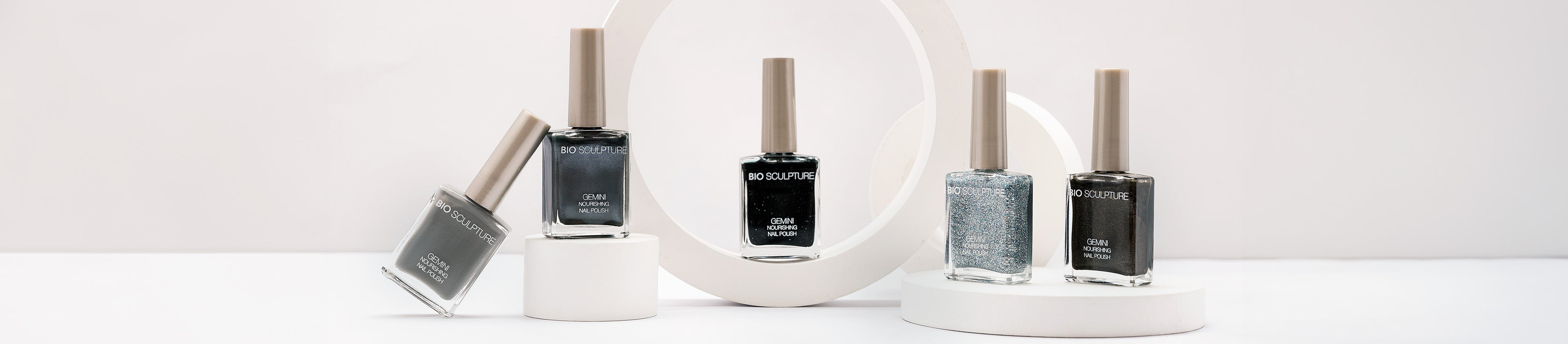 Fünf Flaschen GEMINI Nagellack stehen auf unterschiedlichen Objekten